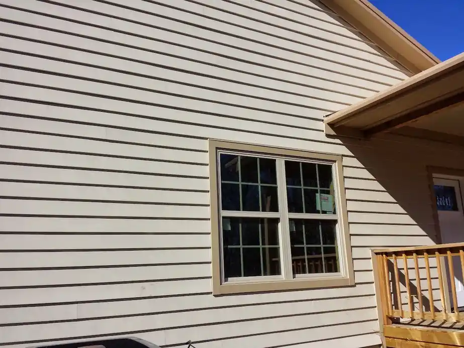 Cream lap siding around a double-hung window beside a porch rail