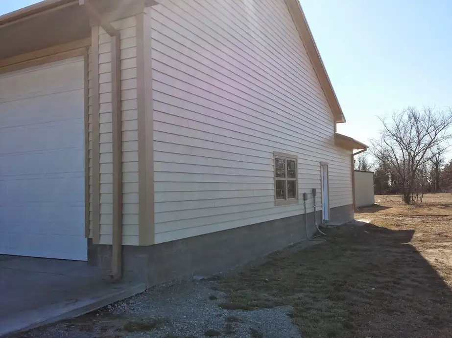 The side of a building with a garage door and fresh siding over a block footing