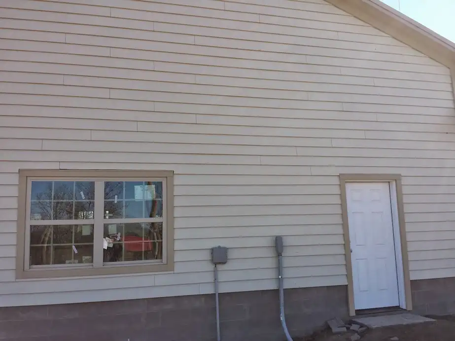 A white entry door and a double-hung window set into new cream lap siding above a block footing