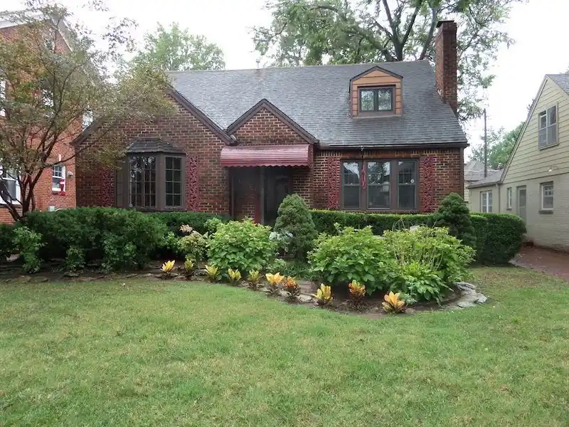 A brick bungalow with a red awning and a landscaped front yard