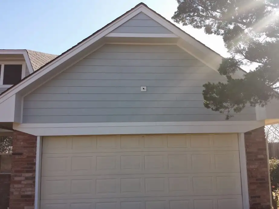 A grey-blue gable above a double garage door with sun flare