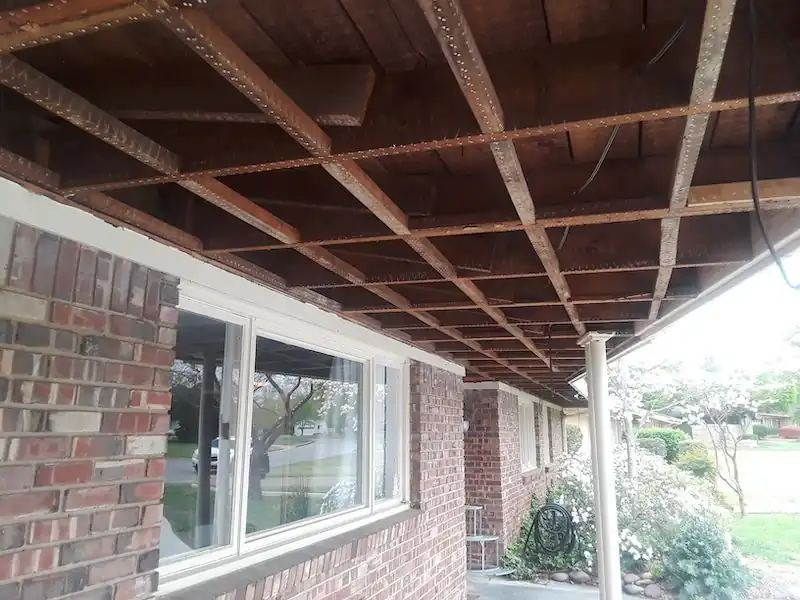 Open soffit framing over a brick wall and picture window, the old covering removed so the joists are exposed