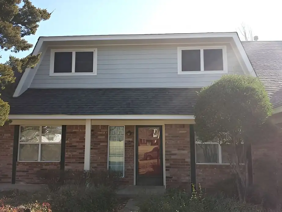 A split-level brick home with its upper storey finished in blue-grey siding and crisp white window trim